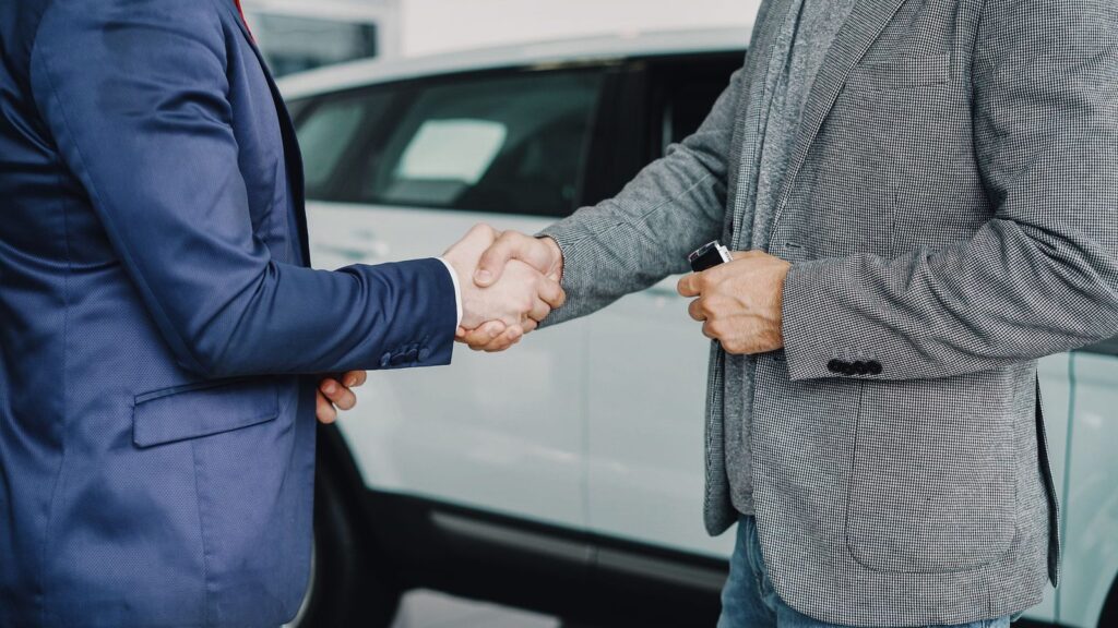 Dos personas se dan la mano delante de un coche blanco